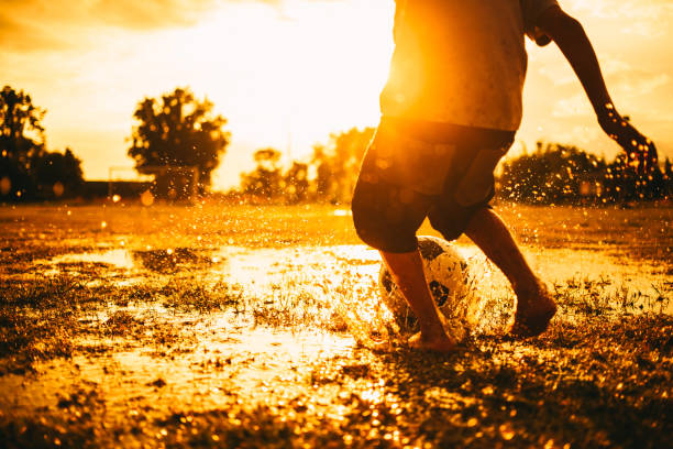 演習では夕暮れの雨のフィールドでサッカーをプレーする子供のシルエット アクション スポーツ写真。 - soccer field dirty soccer outdoors ストックフォトと画像