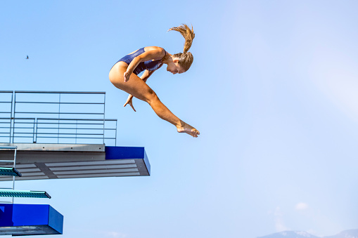 Low angle view of  a female springboard diver in mid-air, springboard and blue sky in backgrounds, copy space.