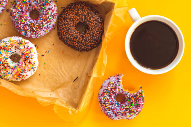 istock Delicious glazed donuts in box and cup of coffee on yellow surface 1090158918