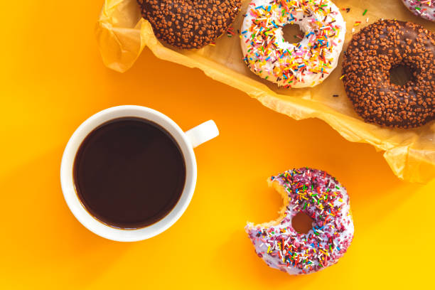 istock Delicious glazed donuts in box and cup of coffee on yellow surface 1090159262