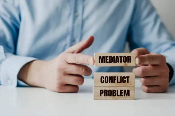 Businessman in a blue shirt arranges wooden jigsaw blocks with the word CONFLICT, MEDIATOR. Problem solving concept using a mediator, help during conflicts.