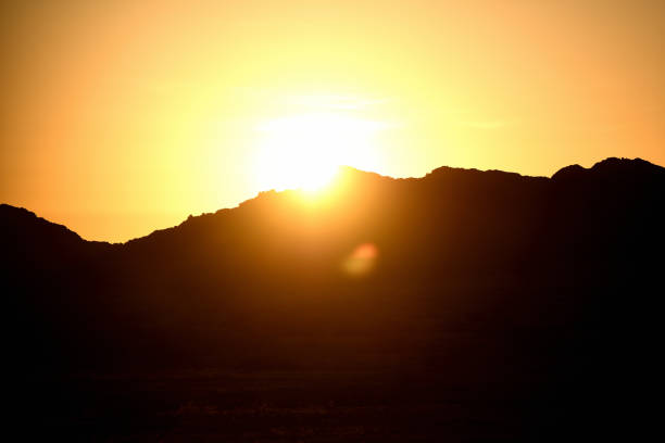The sun is low and in centre of the photo. It is setting behind some mountains which are silhouette.d The sky is orange and the photo is two toned - orange of the sunset, and black of the silhouettes.The photo was taken in the Erongo region of Namibia.  The photo was taken in February 2018.