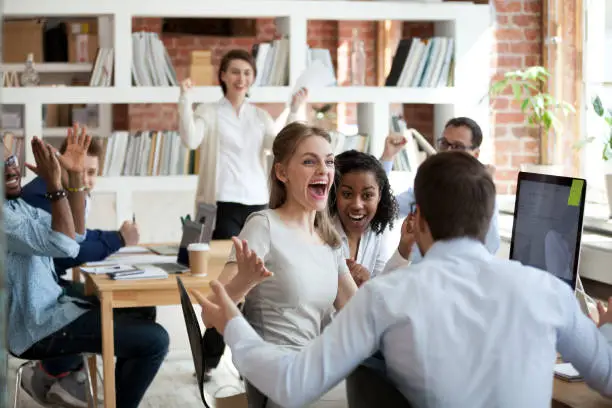 Photo of Excited diverse business team employees screaming celebrating good news success