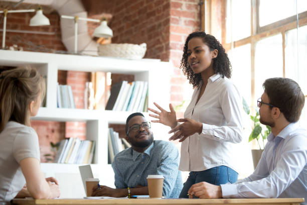 Ambitious african black female employee speaking at diverse meeting Ambitious smart african black female employee speaking at diverse meeting share creative idea opinion at group briefing while jealous envious skeptical male coworkers looking listening to colleague respect stock pictures, royalty-free photos & images