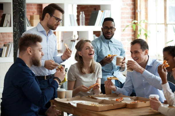 Happy diverse team people talking laughing eating pizza in office Happy diverse team people talking laughing at funny joke eating ordered pizza in office, friendly employees group enjoy positive emotions sharing lunch together having fun at work break on friday business party stock pictures, royalty-free photos & images