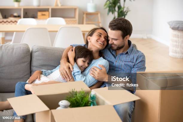 Family With Kid Embracing On Sofa Moving In New Home Stock Photo - Download Image Now