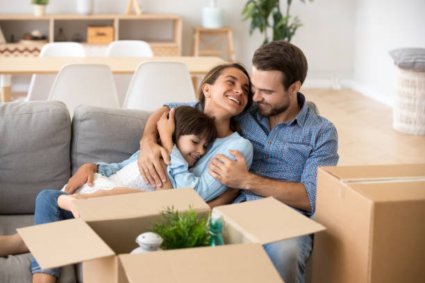 family with kid embracing on sofa moving in new home - moving house apartment couple box imagens e fotografias de stock