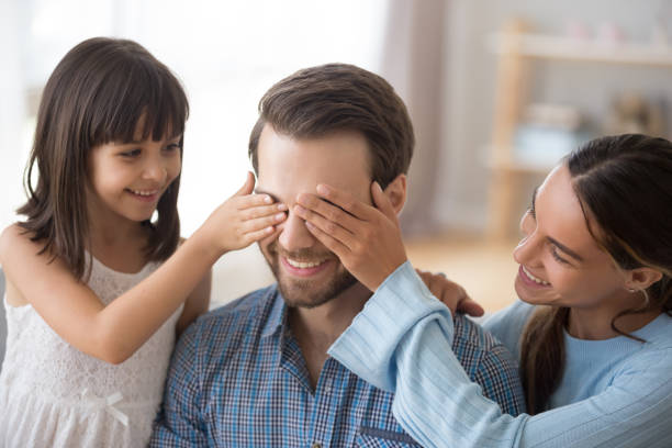istock Wife with kid closing eyes of smiling daddy make surprise 1090217552