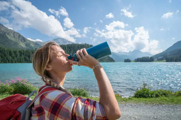 Photo of Hiker woman drinking on mountain lake trail from water bottle