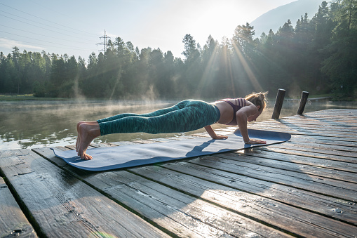 One young woman exercising yoga on a lake pier in the morning, fog on water surface. People wellbeing relaxation healthy lifestyle concept.\nShot in Graubunden Canton, Switzerland.