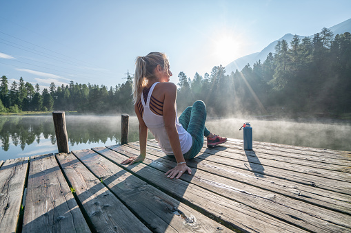 Jogging woman relaxing on lake pier at sunrise enjoying freshness from nature