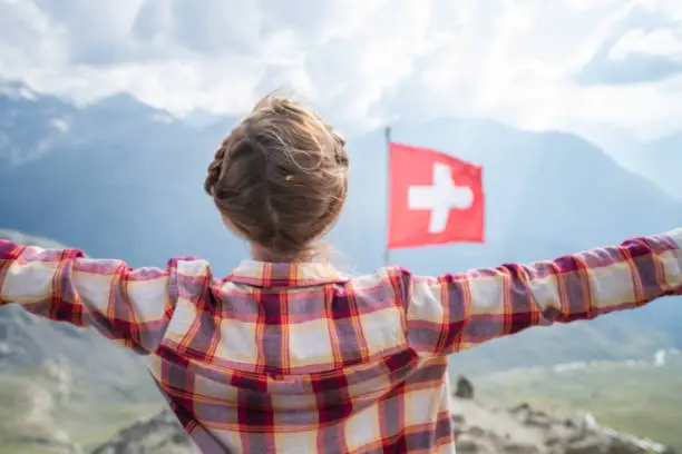 Success on mountain top
Young woman hiking reaches the mountain top, outstretches arms for success and freedom; Swiss flag beside her