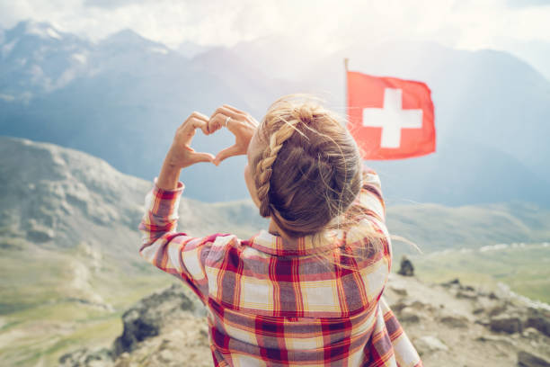 jeune femme faisant le cadre de doigt de forme de coeur sur le sommet de montagne surplombant les alpes suisses; drapeau suisse - european alps women summer outdoor pursuit photos et images de collection
