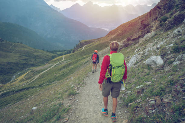 Two hikers walking down the mountain trail in Summer at sunset
