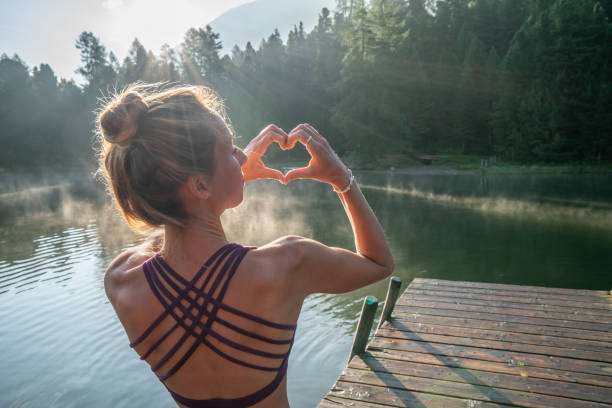 fille de yoga sur la jetée du lac au lever du soleil faisant un cadre de doigt de forme de coeur sur le beau paysage - st moritz mountain nature water photos et images de collection