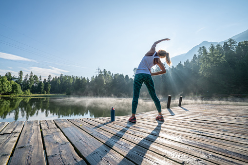Young woman stretching body before morning jogging, sunrise over beautiful peaceful lake in nature, female standing on pier over water
Shot in Graubunden Canton, Switzerland.