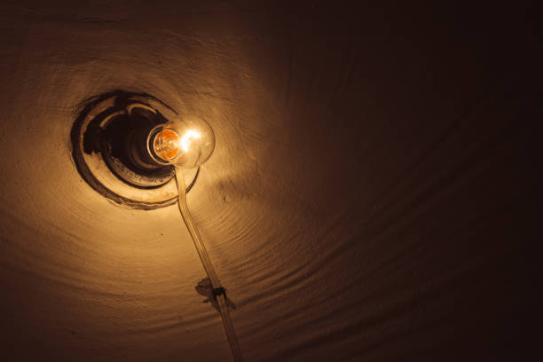 istock Incandescent lamp burns inside dark room close-up. Illumination with copy space. Old light bulb on rough wall. Lamp illuminate basement. Light in darkness. Minimalist background. Warm orange lighting. 1090262554