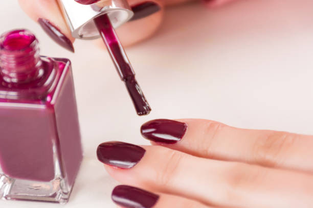 Female with paint brush and bottle applying red wine manicure nails polish on finger stock photo