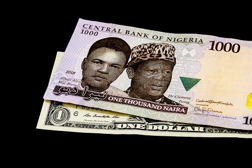 A Thousand Nigerian Naira Note on a US Dollar Bill, Isolated on a Black Background