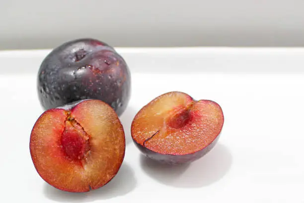 Plum Cut Open in Two Halves, Sliced Fruit on a White Surface