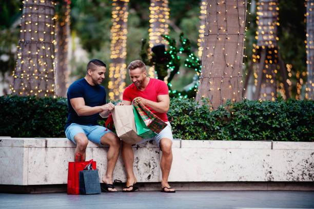 Christmas summer with multi-ethnic gays Christmas summer in Miami Florida with two gays multi-ethnic. 1 caucasian and 1 latino. They shop in stores. Two men looking at their purchases. Looking in shopping bags. Opening gift bags side by side. Loving adult gays together. They are bonding and having a great moment. Beautiful Christmas lights. florida christmas stock pictures, royalty-free photos & images