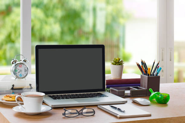 Home office workplace with mockup laptop (with blank screen for montage), notebook, tea cup, clock and stationery on wooden desk. Good morning, Fresh start, Start up or Start working concept. stock photo