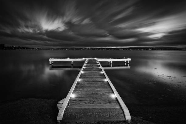 Timber jetty lined with night lights and a moody cloudy sky at night.  Long exposure