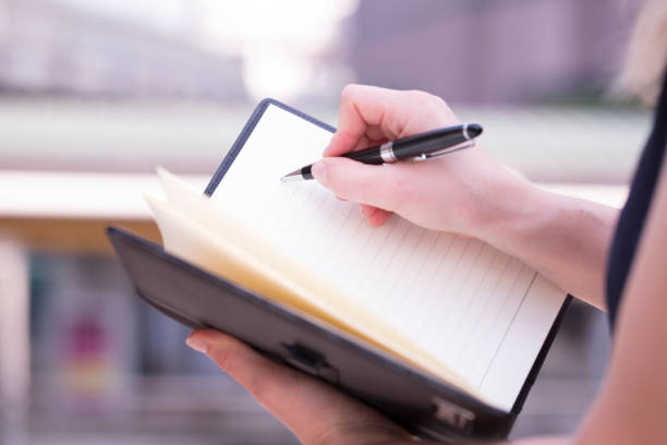 istock Hand holding luxury pen and writing on white blank notebook, with beautiful daylight blurry background. 1090353348