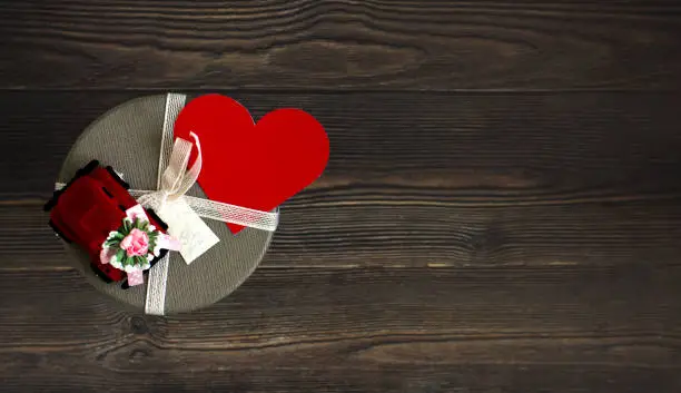 Gift box with red heart on the top on wooden surface