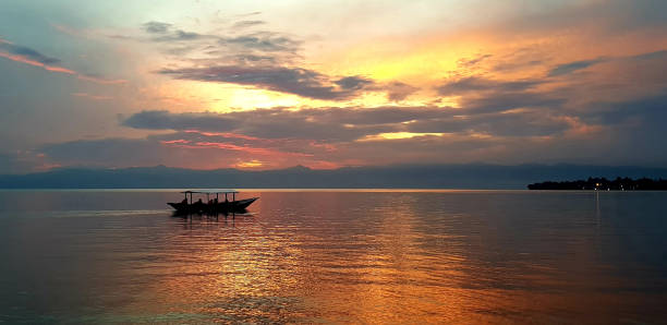 Boat Sailing on Lake Kivu, Rwanda, with Fiery Sunset Backdrop A boat sailing in the sunset on Lake Kivu in Rwanda, East Africa; A part of Lake Kivu is also found in Congo, and the Lake provides a source of income for fishermen. lake kivu stock pictures, royalty-free photos & images