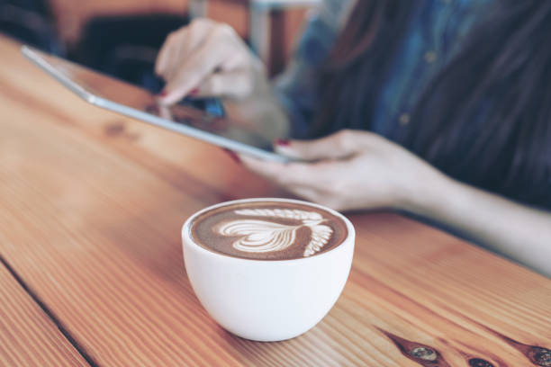 istock white coffee cup with latte art heart pattern on a wooden table background and Young woman hand holding smartphone in a  coffee shop cafe 1090380452