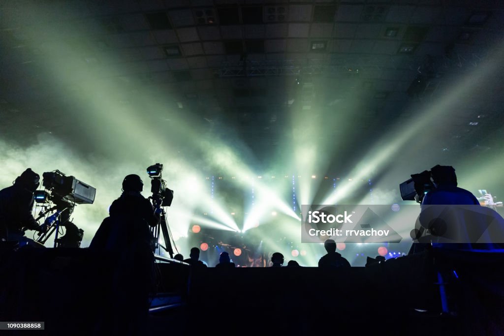 Silhouette of a group of cameramen broadcasting an event. Silhouette of a group of cameramen broadcasting an event. Workers are on a high platform on the background of bright beams. Event Stock Photo