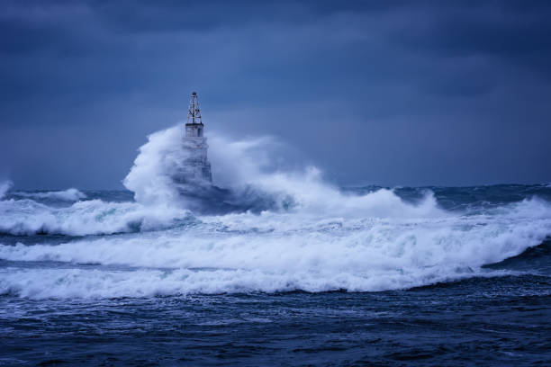 big wave against old lighthouse in the port of ahtopol, black sea, bulgaria on a moody stormy day. danger, dramatic scene. - storm lighthouse cloudscape sea imagens e fotografias de stock