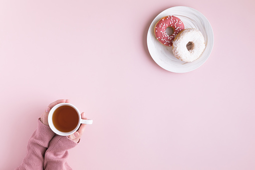 Morning coffee cup and sweet donut on pink pastel table, top view. Flat lay of cozy breakfast