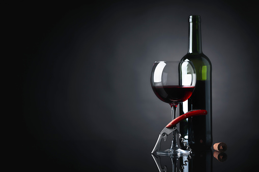 Glass and bottle of red wine with corkscrew on a black reflective background. Copy space for your text.