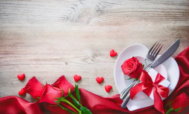 Plates in shape of heart, holidays table setting with a gift box on wooden table. Valentines day concept