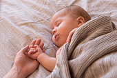Close-up of sleeping baby hand in the mother's hand on the bed. New family and baby sleep concept