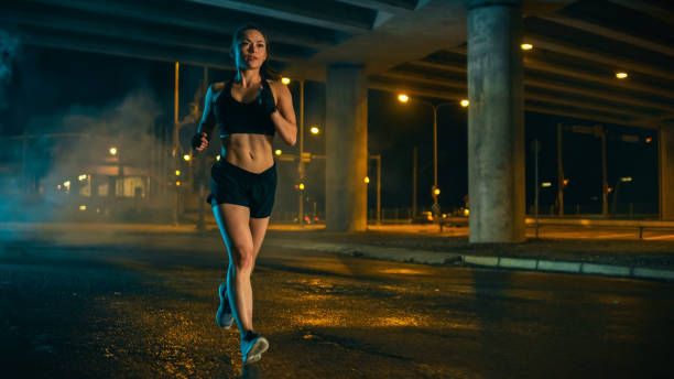 schöne fitness girl in black athletic top und shorts ist jogging auf der straße. sie ist ein training in einen abend nass städtischen umwelt unter a bridge tun. - marathon sport sports training city street stock-fotos und bilder