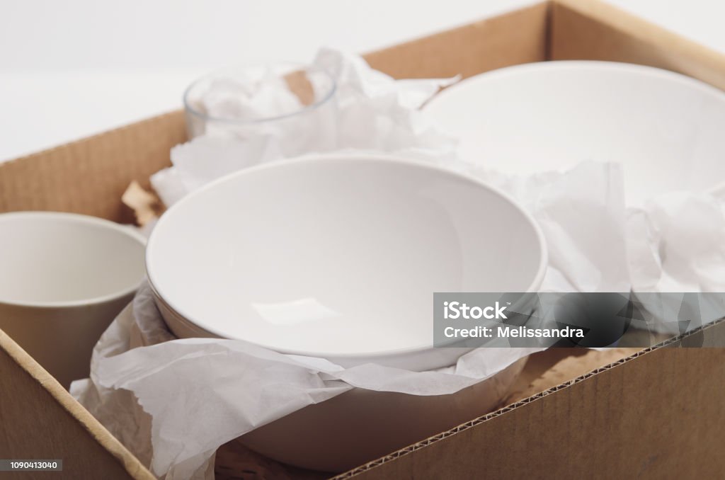 Clean white dishes in paper packed in a cardboard box. Concept relocation Clean white dishes in paper packed in cardboard box. Concept relocation. Plate Stock Photo