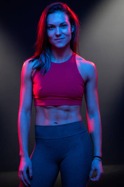Dark moody portrait of fitness model girl relaxing between exercises looking at camera Dark moody portrait of fitness model girl relaxing between exercises looking at camera. The female is of caucasian ethnicity and the shot takes place indoors on a black studio backdrop in Sofia, Bulgaria. The picture is taken with Sony A7RIII camera. crossfit girl stock pictures, royalty-free photos & images