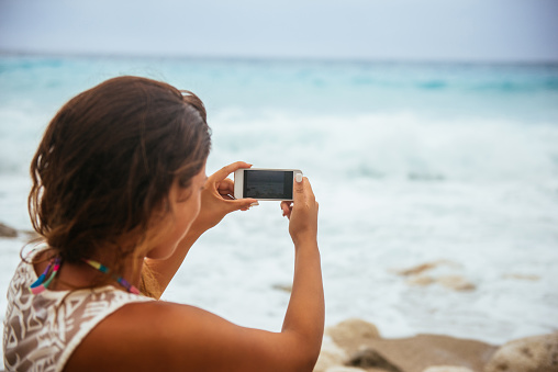 Beautiful woman taking a photo of an ocean on the beach.