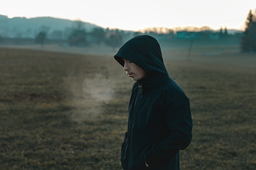thinking teen with hoodie standing outside at field and breathe out