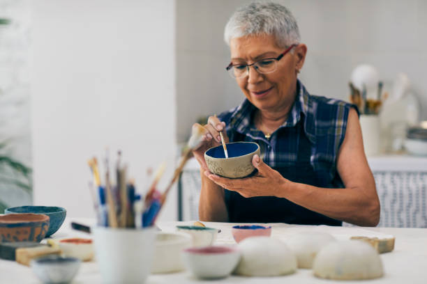 Seniors Ceramic Workshop Senior woman decorating bowl made of clay on ceramics workshop. pottery photos stock pictures, royalty-free photos & images