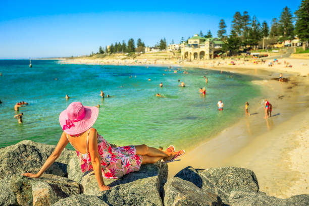 Woman at Cottesloe Beach Woman in hat looking at the turquoise waters of Cottesloe Beach, Perth's most famous town beach, Western Australia. Girl sunbathing on the rocks of the Indian Ocean. Summer season with blue sky. cottesloe beach stock pictures, royalty-free photos & images