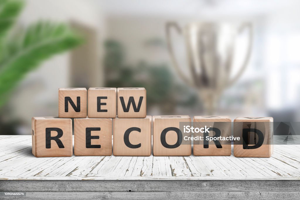 New record sign on a wooden table in a bright room New record sign on a wooden table in a bright room with green plants and a trophy Record - Analog Audio Stock Photo