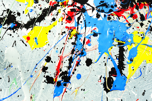 a spot of white and black and yellow and green and red and blue spilled paint on a concrete textured surface.