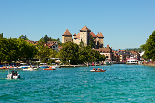 Boats and pedal boats on the Lake of Annecy on summertime with the castle in the background.