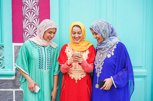 Happy islamic frends using smartphone - Young arabian girls having fun with new social app outdoor - Technology, influencer and friendship concept - Focus on faces