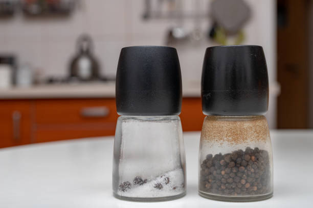 Salt and pepper in containers on the kitchen table. Spices in the home kitchen. Light background.