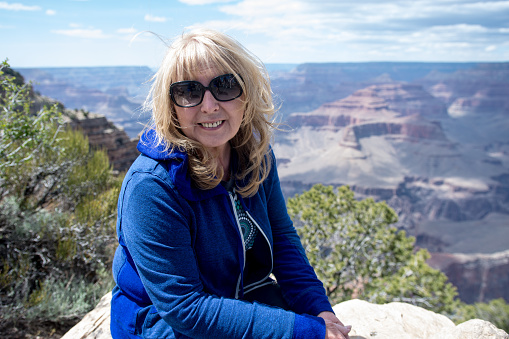 Senior adult woman (60s) sits and poses at a viewpoint along the South Rim of the Grand Canyon National Park while on vacation
